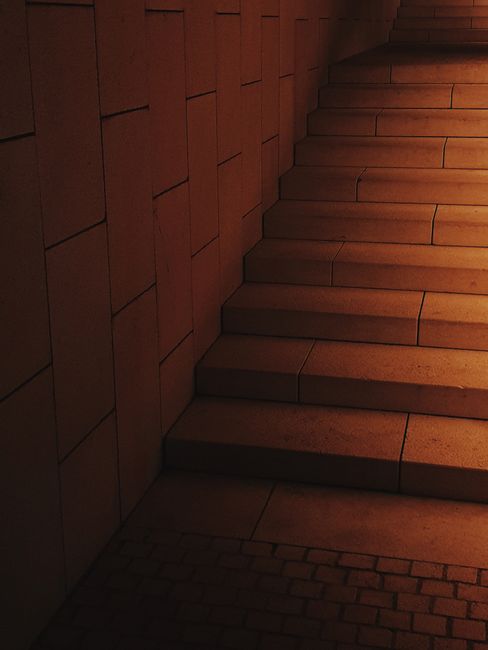 A professional furniture removal process inside a residential property, showing a person carefully maneuvering a large cardboard box wrapped in plastic film through a narrow staircase. The stairwell i